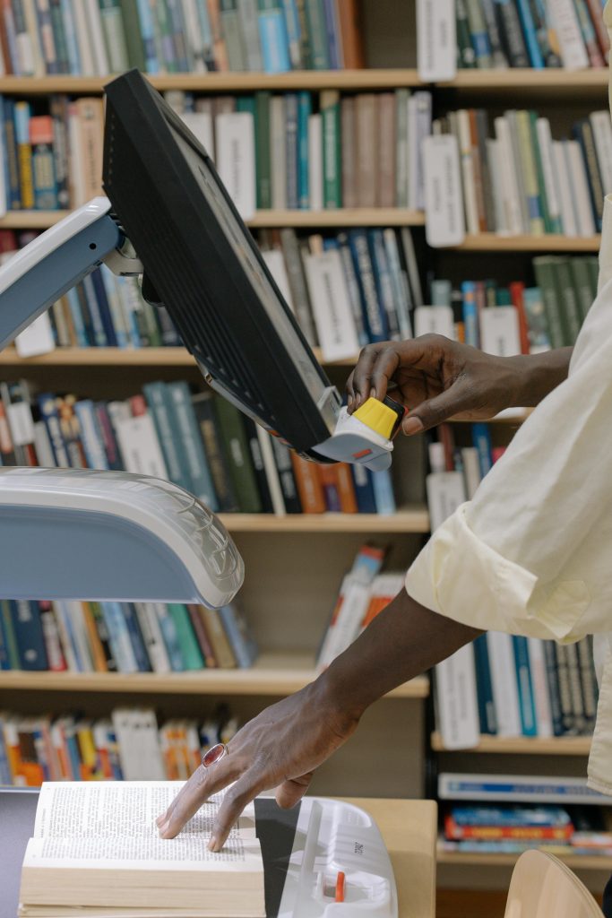 pexels-photo-6334791-6334791 Hands scanning a textbook in a modern library, showcasing technology and learning resources.